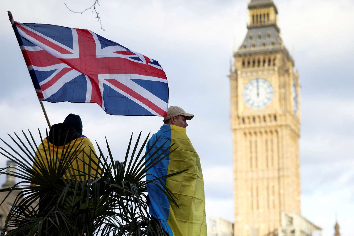 People wrapped in Ukrainian flags beneath a Union flag outside the Houses of Parliament in London