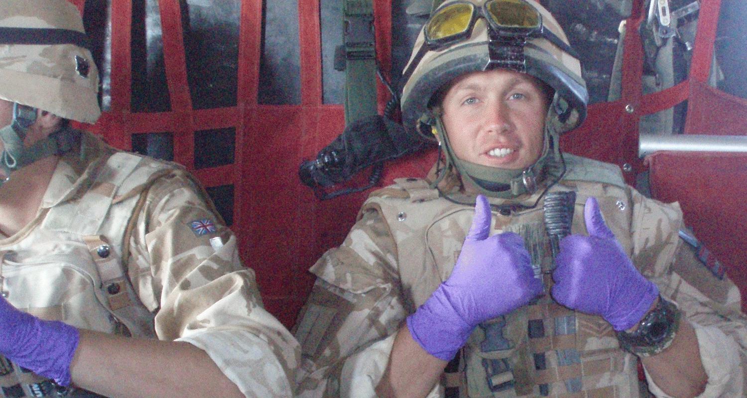A British soldier in desert combat dress seated in the back of a transport helicopter on deployment